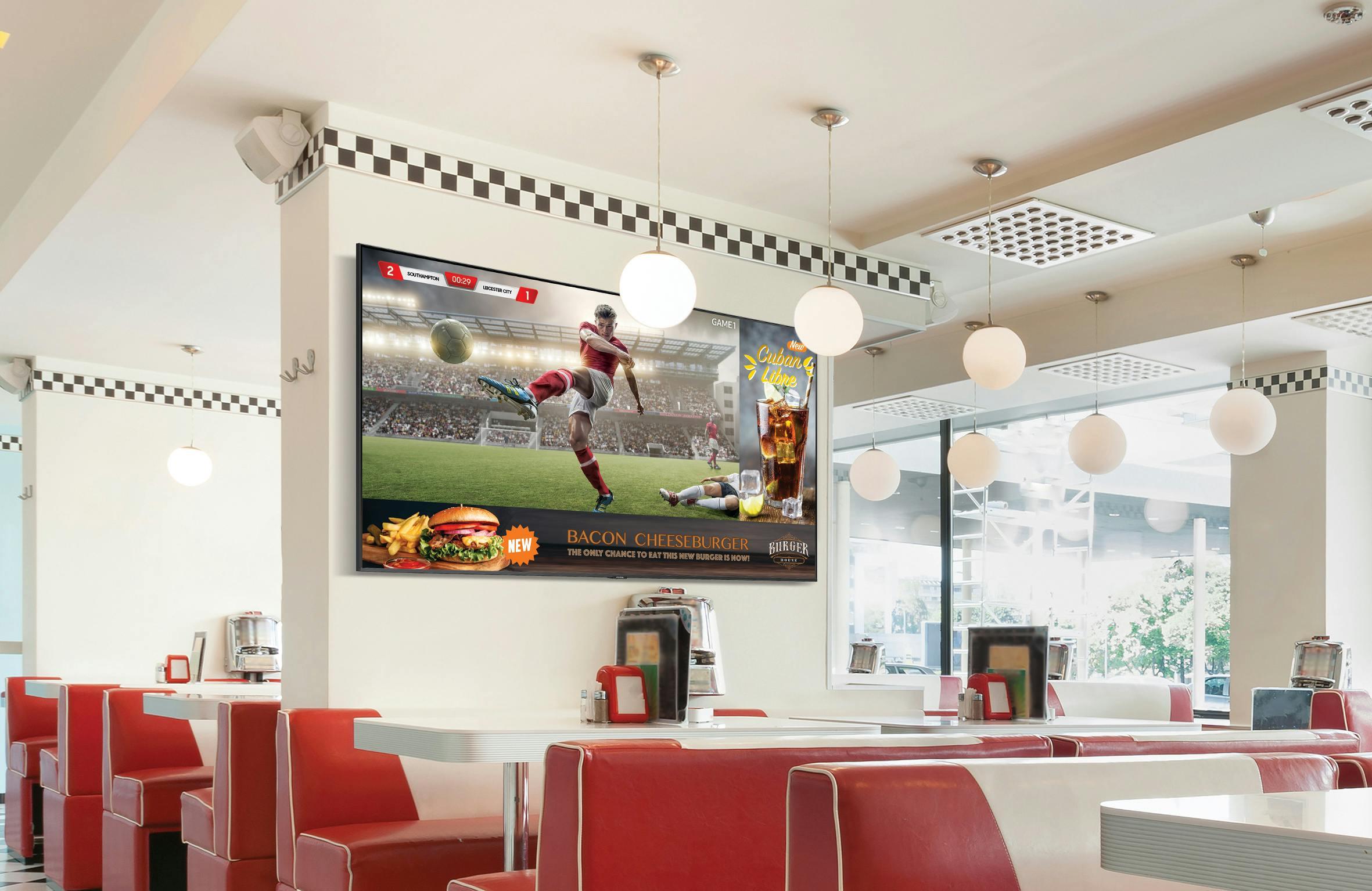 A soccer match is played on screen while restaurant specials appear on the bottom inside a fast-food restaurant